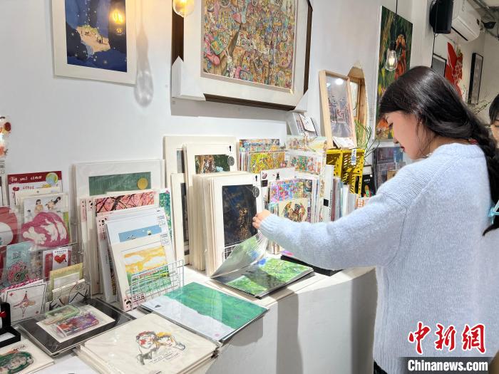 圖為藝術(shù)品商店內(nèi)，顧客挑選插畫作品?！＄婌?攝